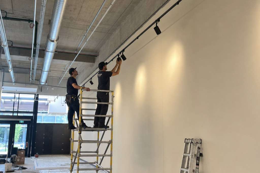 Two technicians on a mobile tower aiming track-mounted spotlights in an interior still being finished