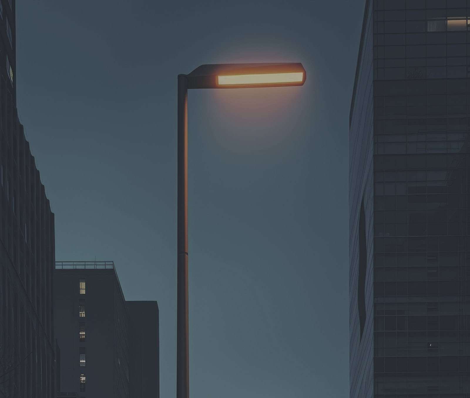 A single lit smart light pole standing between city towers at dusk